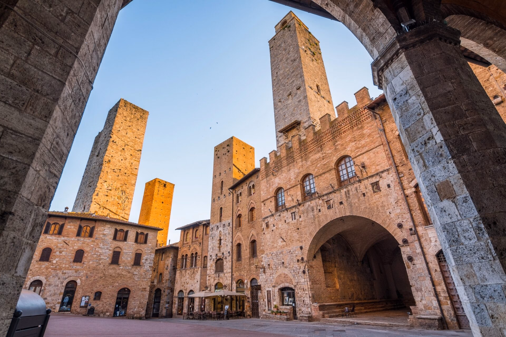 Piazza del Duomo in San Gimignano in golden light seen through a stone arch