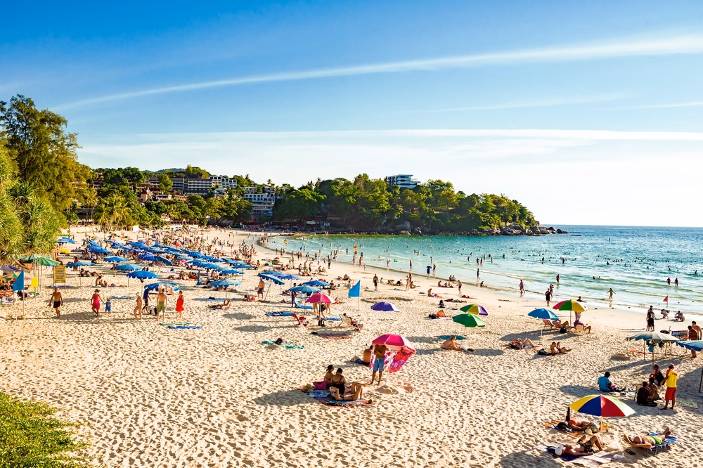 Spacious Kata sandy beach on Phuket in Thailand on a sunny day. Tourists swim in the turquoise sea and relax under colourful parasols.