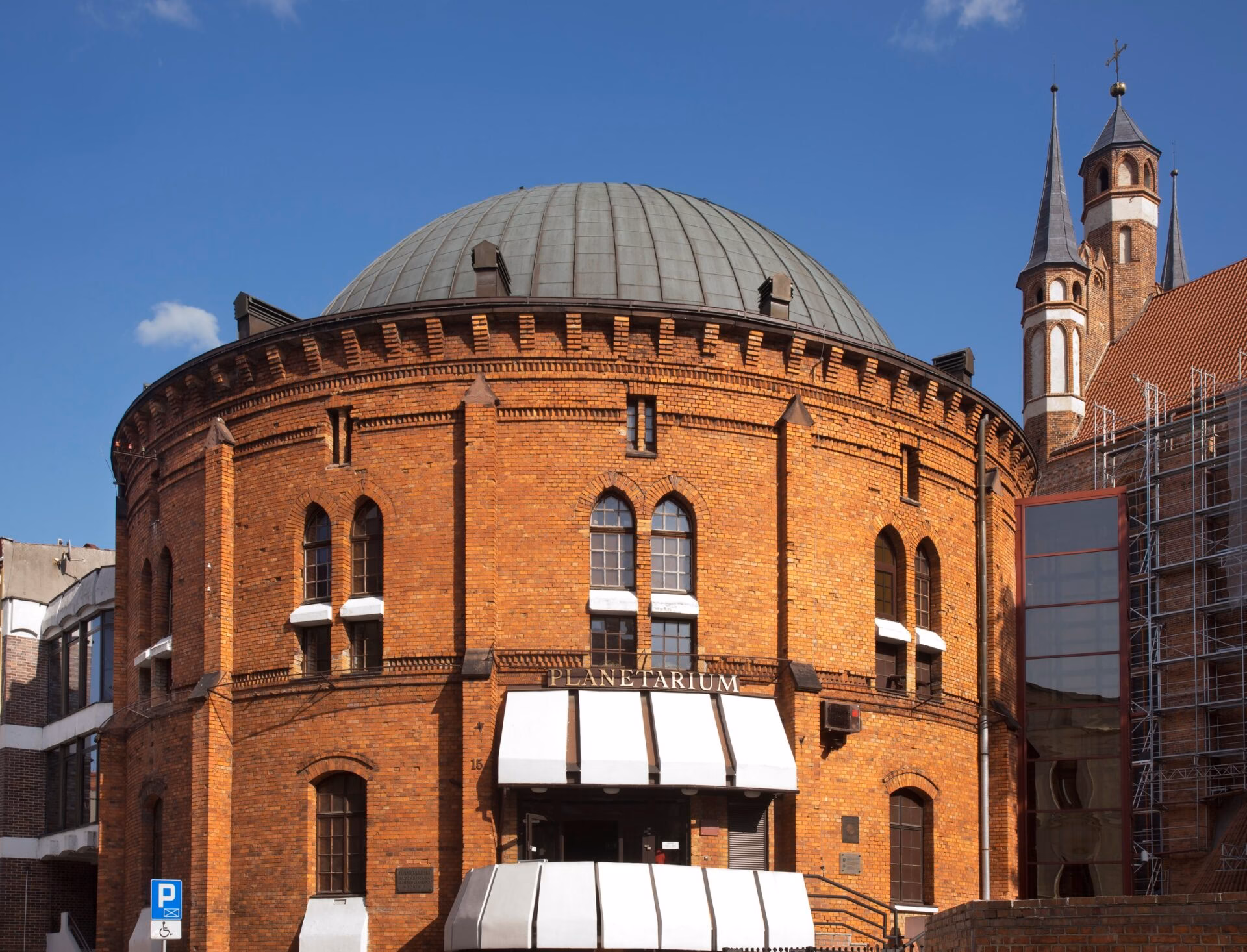 Round brick planetarium building with a dome and church towers in the background in Toruń