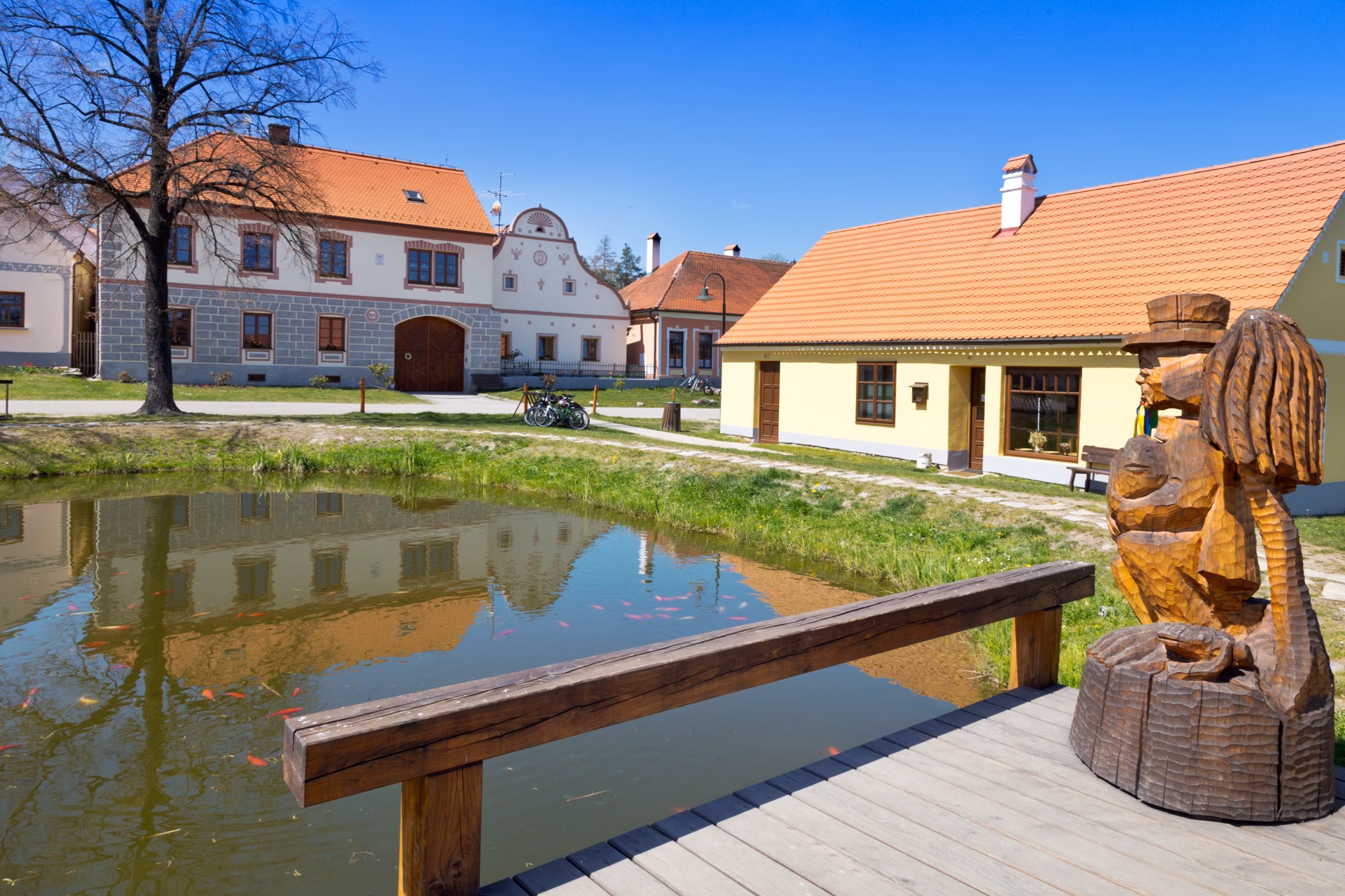 A jetty with a wooden water-sprite statue by the village pond in Holašovice