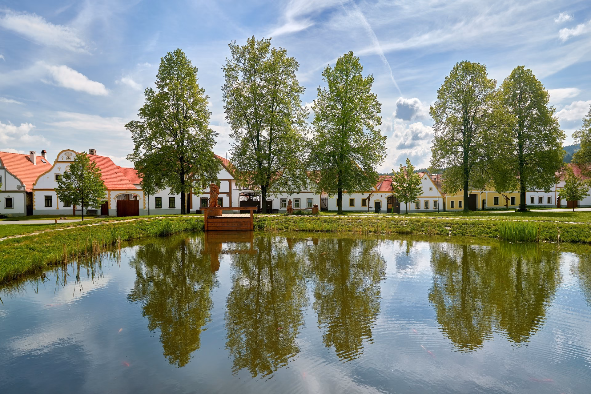 The village pond in Holašovice reflecting the farmsteads and lime trees on its surface