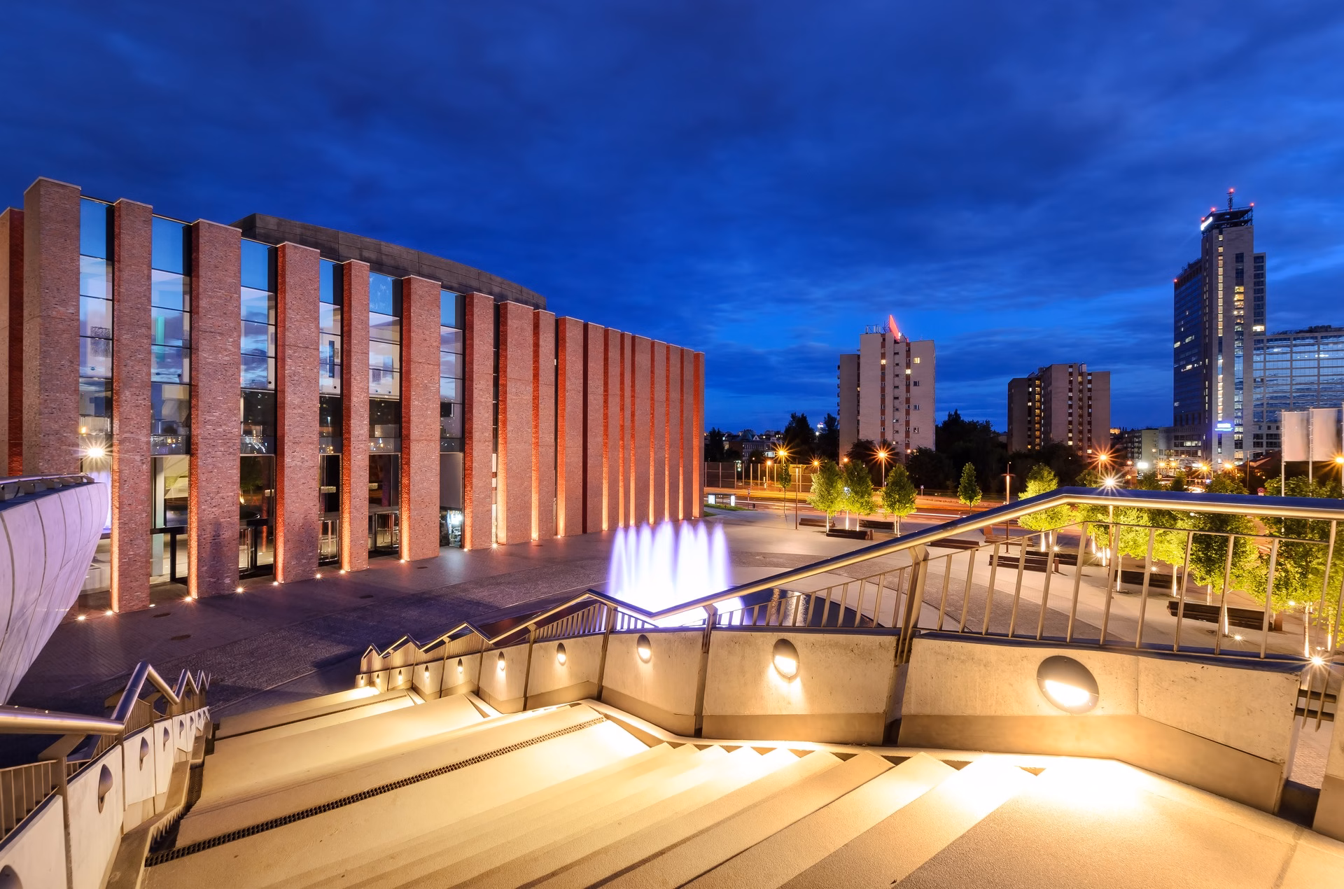 The NOSPR building in Katowice in the evening, brick pillars and an illuminated fountain